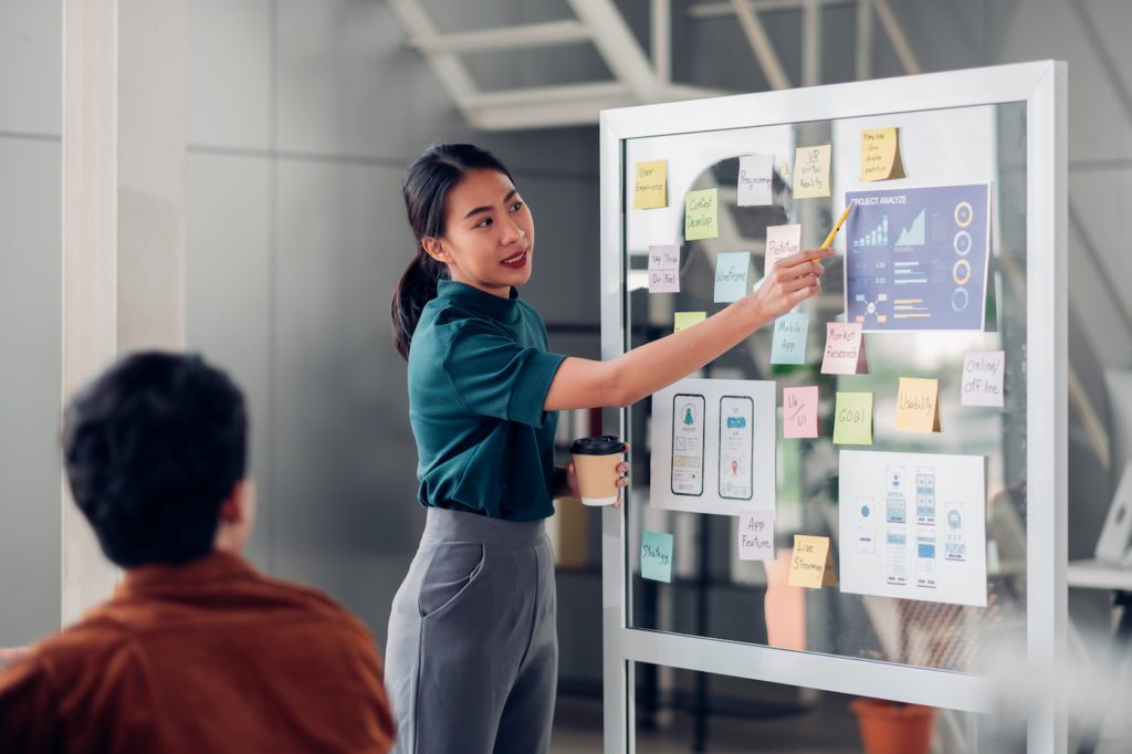 Business woman at a whiteboard collaborating with a colleague. Represents tips for IT department transformation.